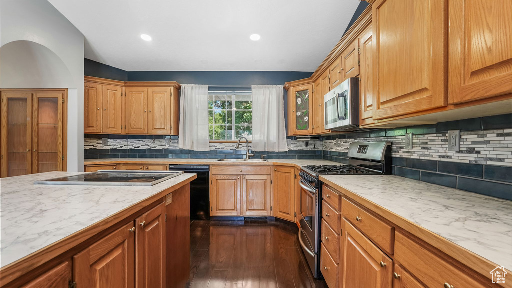 Kitchen featuring appliances with stainless steel finishes, dark wood finished floors, light countertops, a sink, and backsplash