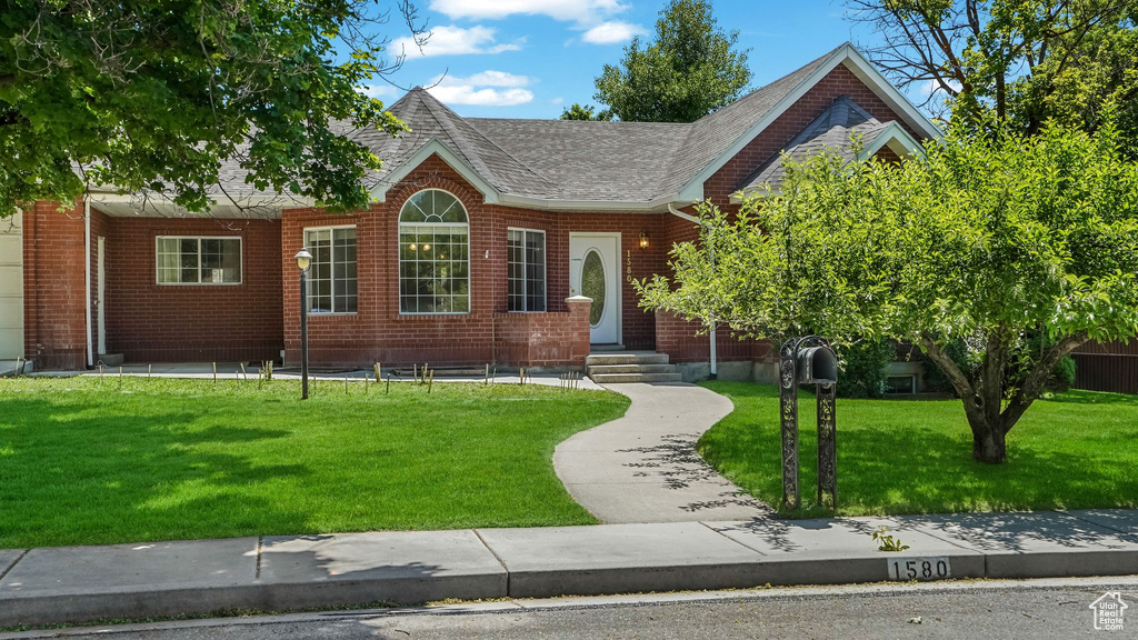 View of front of property with a front lawn, roof with shingles, and brick siding