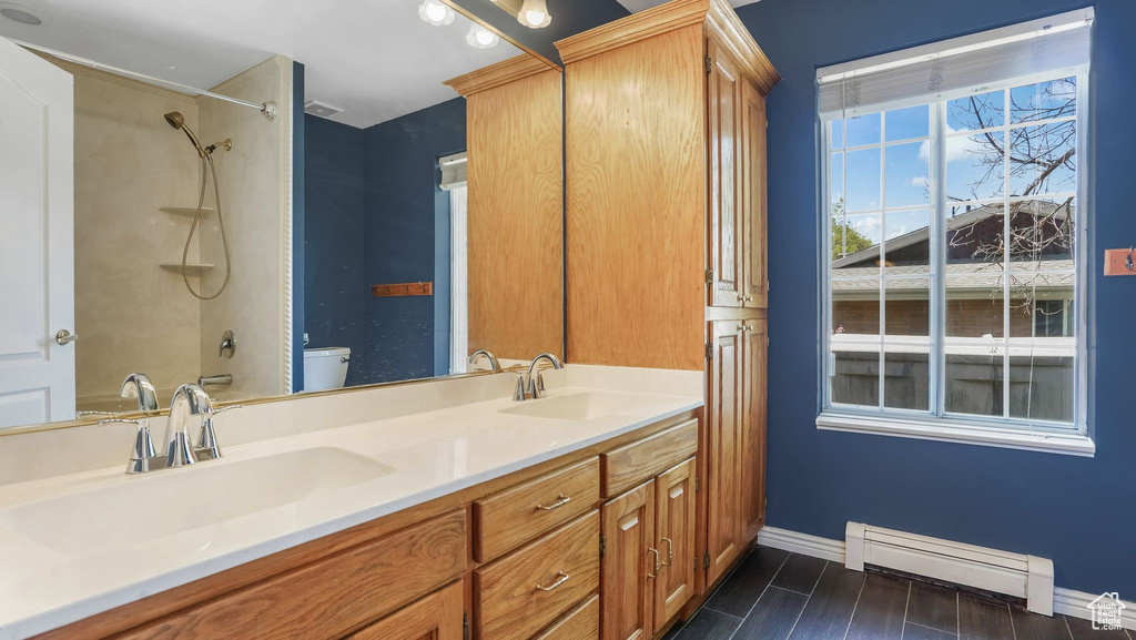 Bathroom featuring baseboard heating, toilet, baseboards, double vanity, and a shower