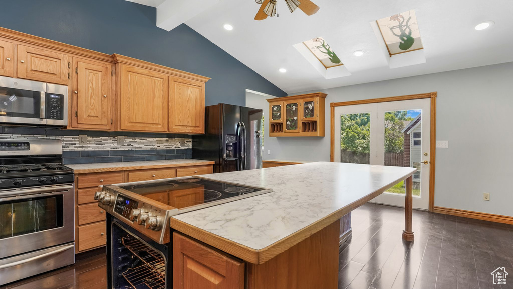 Kitchen with appliances with stainless steel finishes, a skylight, light countertops, tasteful backsplash, and a kitchen island