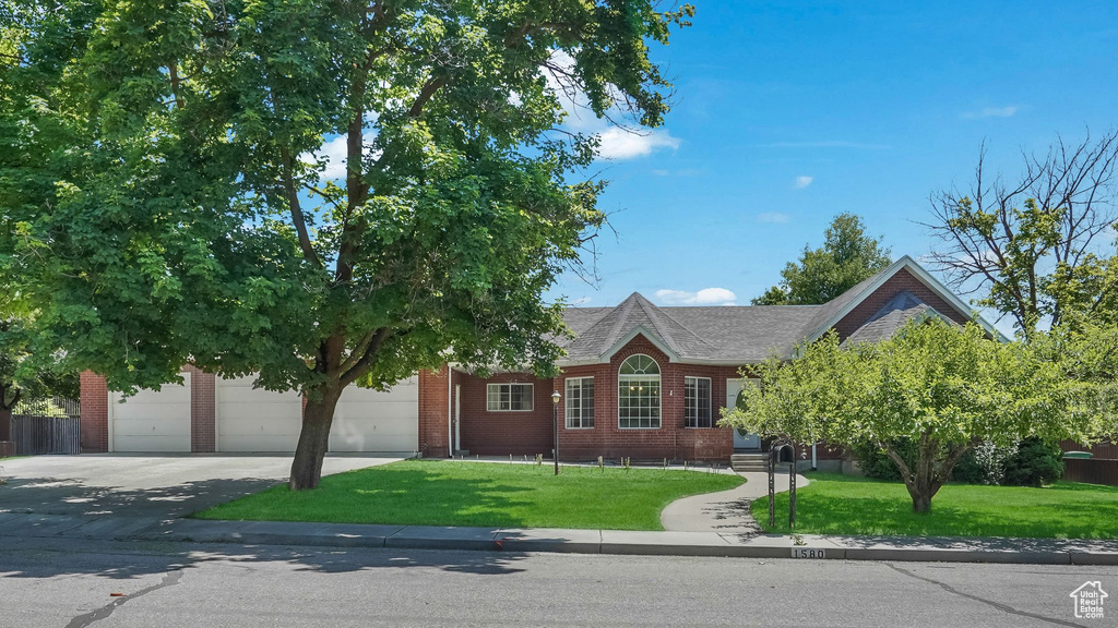 View of front of property featuring concrete driveway, brick siding, a front yard, and a garage