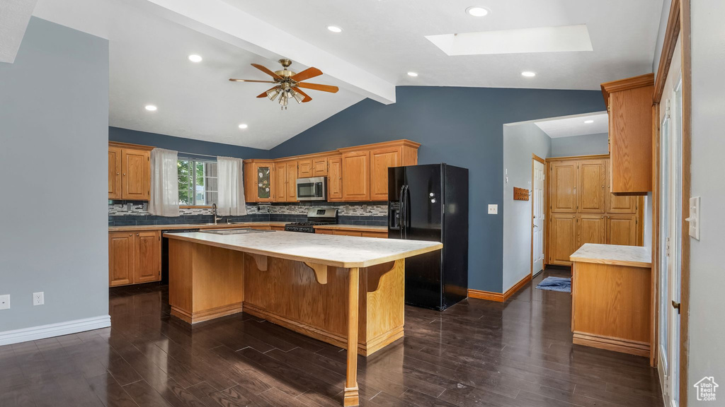 Kitchen featuring appliances with stainless steel finishes, dark wood-style flooring, decorative backsplash, a kitchen island, and light countertops