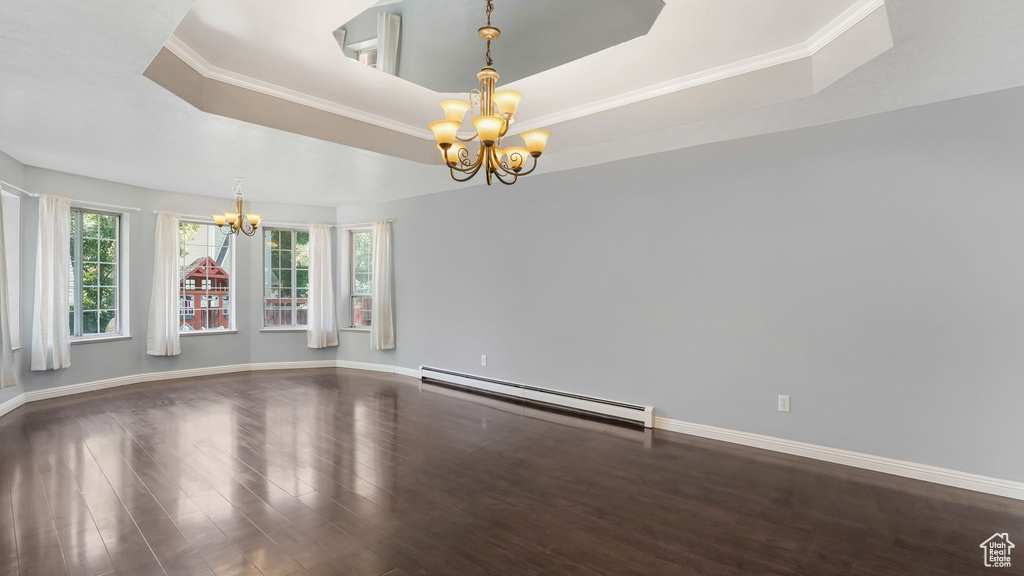 Spare room featuring a chandelier, baseboard heating, wood finished floors, a tray ceiling, and ornamental molding
