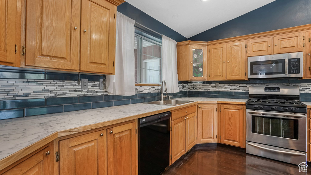 Kitchen featuring appliances with stainless steel finishes, a sink, lofted ceiling, dark wood-type flooring, and light countertops