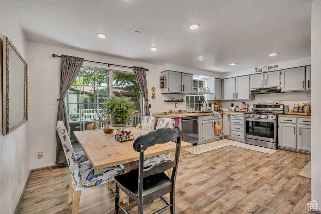 Kitchen with appliances with stainless steel finishes, gray cabinets, exhaust hood, light wood-style floors, and recessed lighting