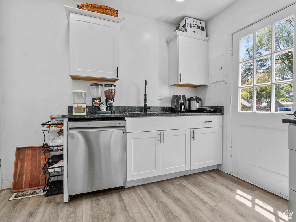 Kitchen with stainless steel dishwasher, a sink, light wood-style flooring, white cabinetry, and dark stone countertops