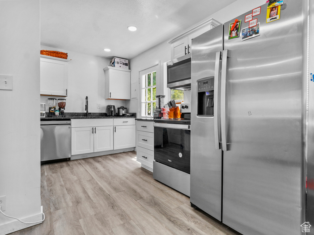 Kitchen with stainless steel appliances, a sink, white cabinets, light wood-style floors, and dark countertops