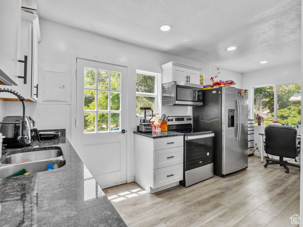 Kitchen with appliances with stainless steel finishes, white cabinets, dark stone countertops, light wood-style floors, and recessed lighting