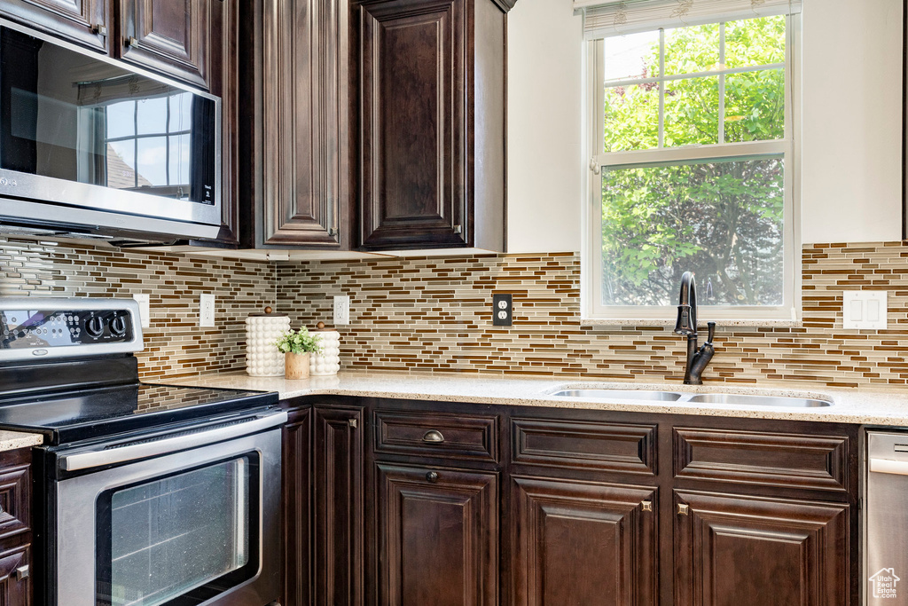 Kitchen with stainless steel appliances, a sink, dark brown cabinets, tasteful backsplash, and light stone countertops