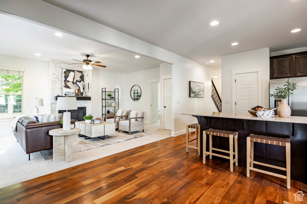 Living room featuring a stone fireplace, wood finished floors, recessed lighting, a ceiling fan, and baseboards