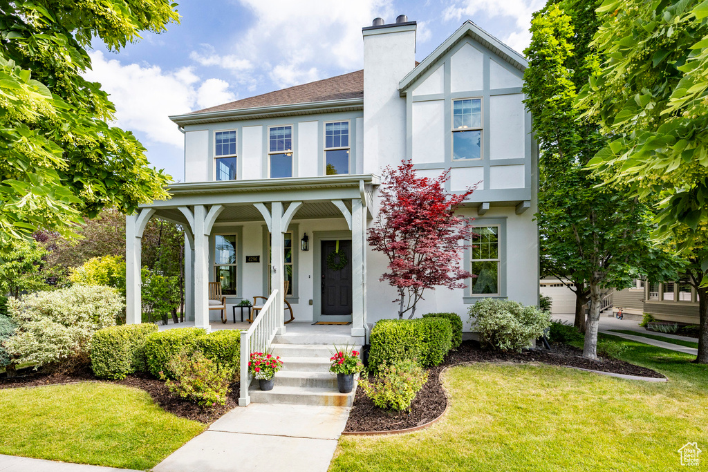 View of front of property featuring stucco siding, covered porch, a chimney, and a front lawn