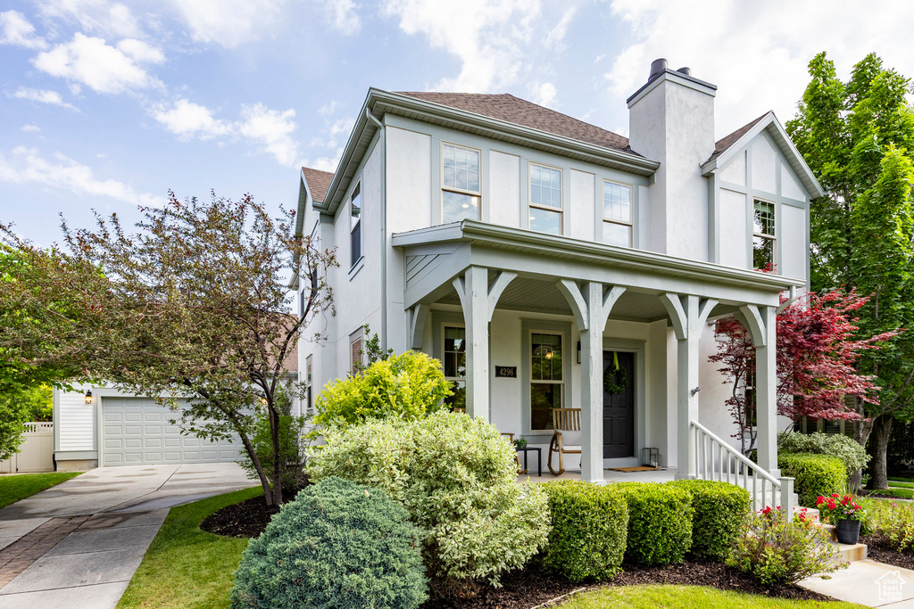 View of front of house with a porch, stucco siding, a garage, a chimney, and concrete driveway