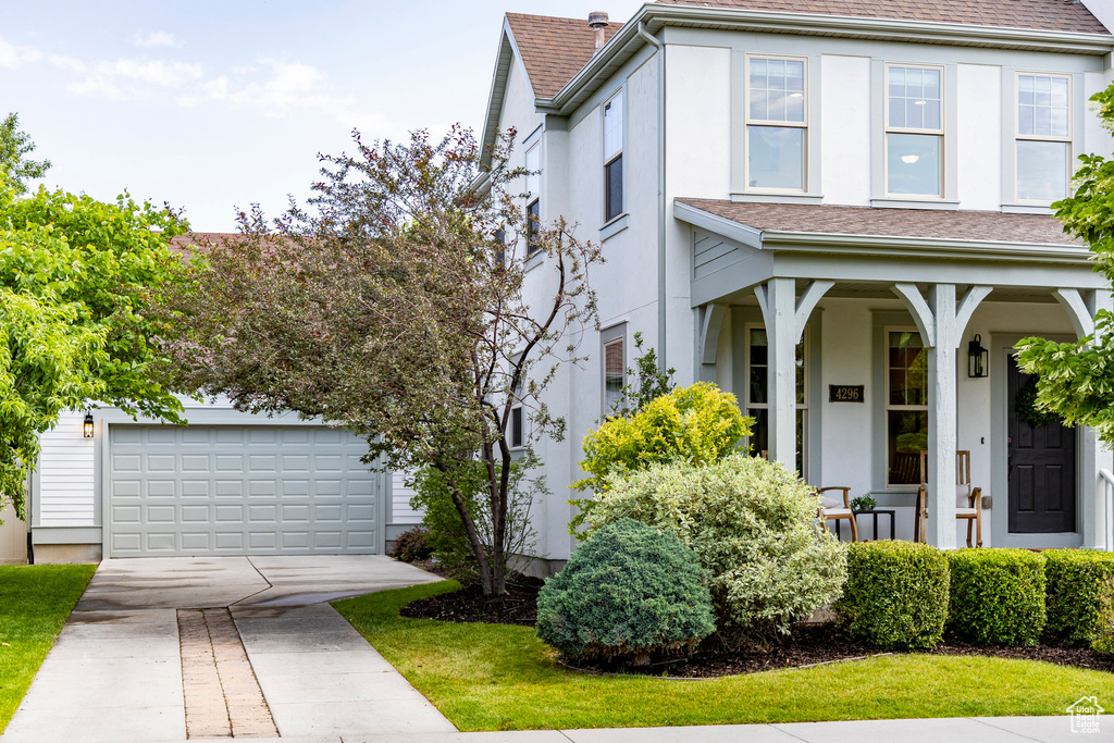 View of front facade with stucco siding, driveway, a garage, covered porch, and a shingled roof