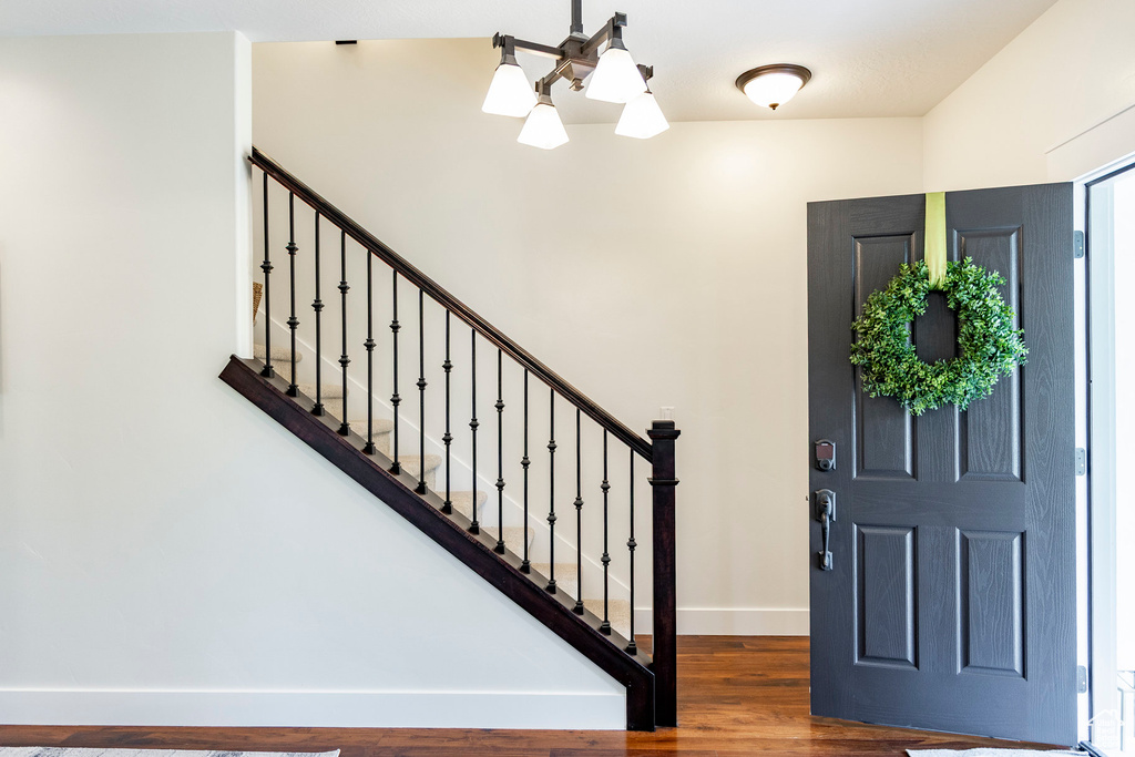 Foyer with baseboards, wood finished floors, stairs, and a chandelier