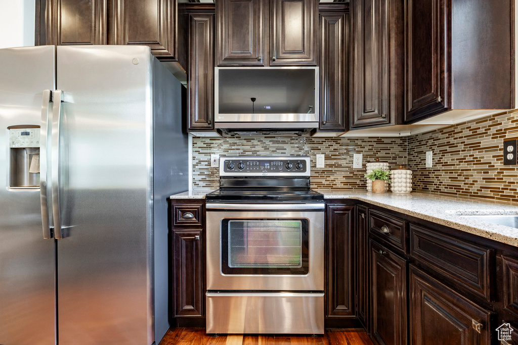 Kitchen featuring stainless steel appliances, dark brown cabinetry, light stone counters, and decorative backsplash