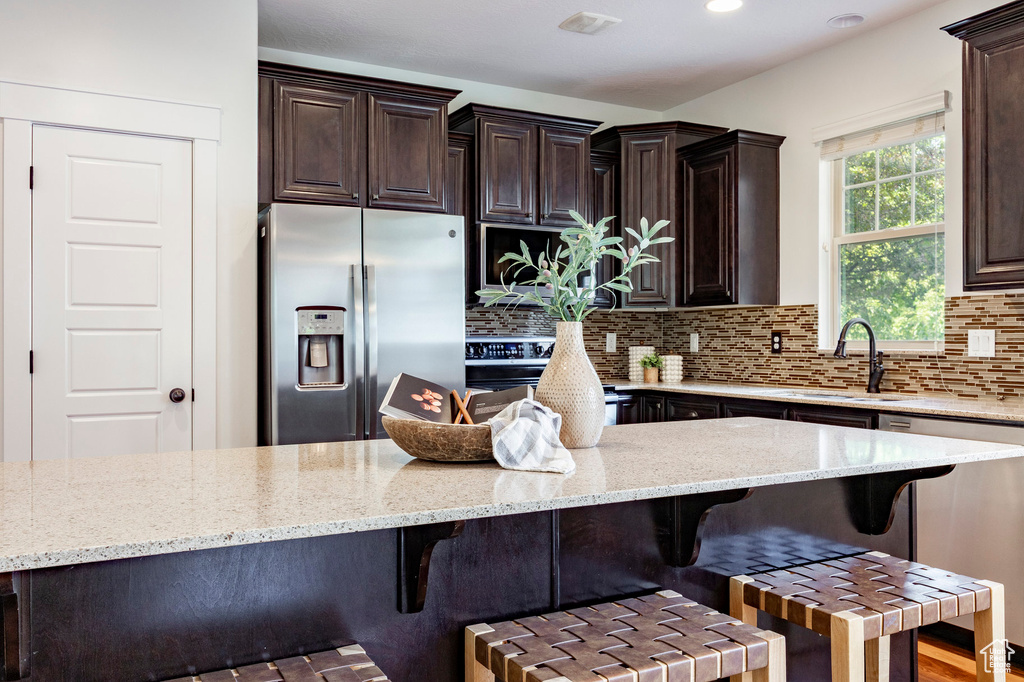 Kitchen with stainless steel appliances, tasteful backsplash, a sink, light stone counters, and dark brown cabinetry