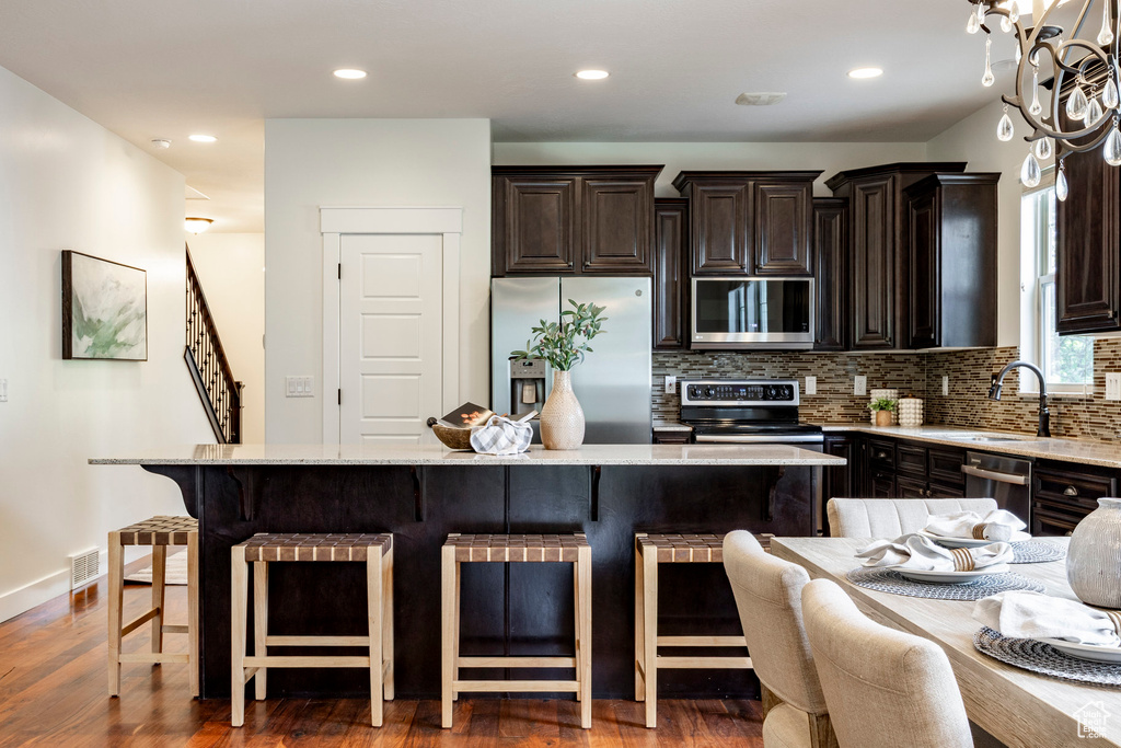 Kitchen with stainless steel appliances, a breakfast bar, a center island, backsplash, and recessed lighting