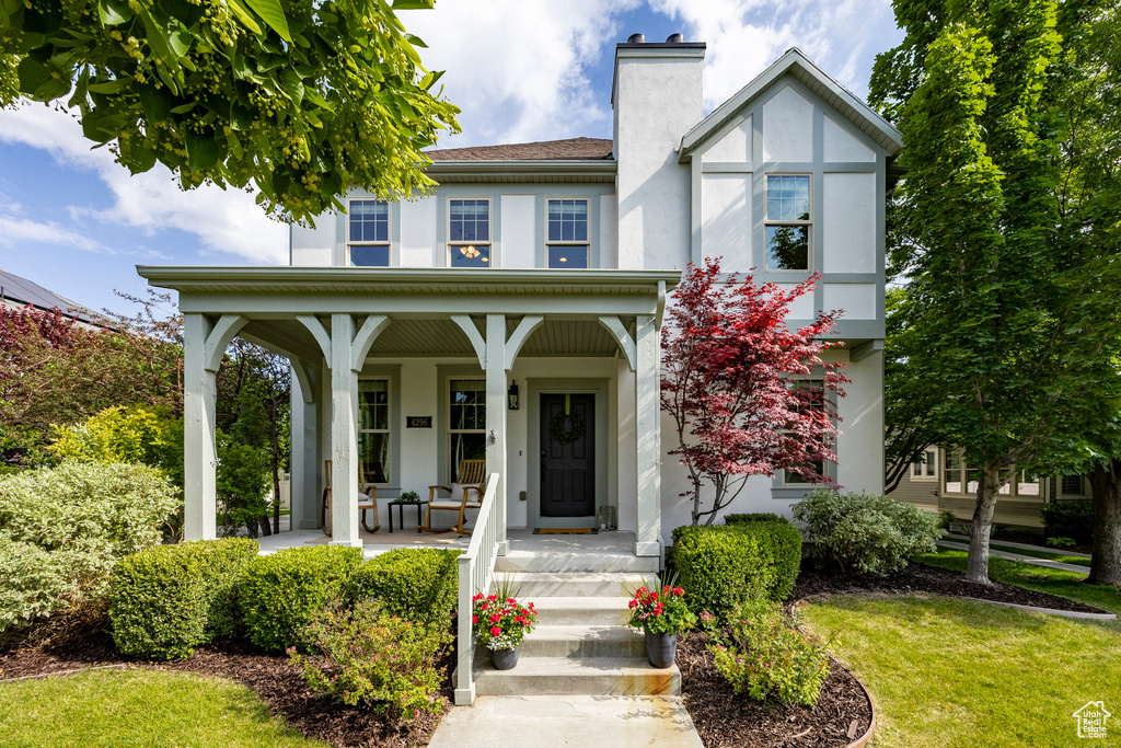 View of front facade featuring stucco siding, covered porch, a chimney, and a front yard