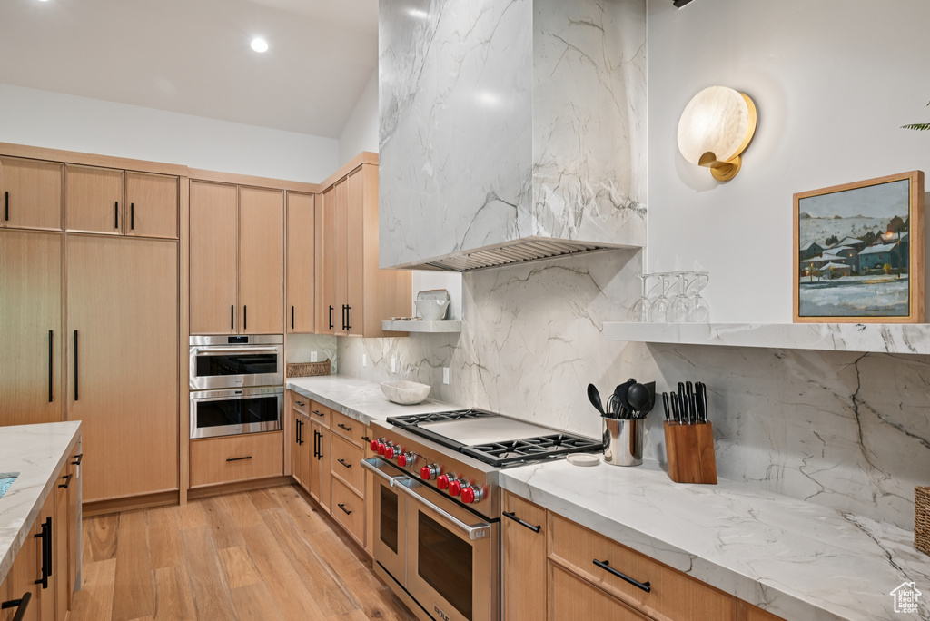 Kitchen with stainless steel appliances, wall chimney range hood, light wood-type flooring, tasteful backsplash, and recessed lighting