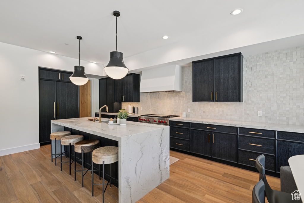 Kitchen with dark cabinets, wall chimney exhaust hood, backsplash, and recessed lighting