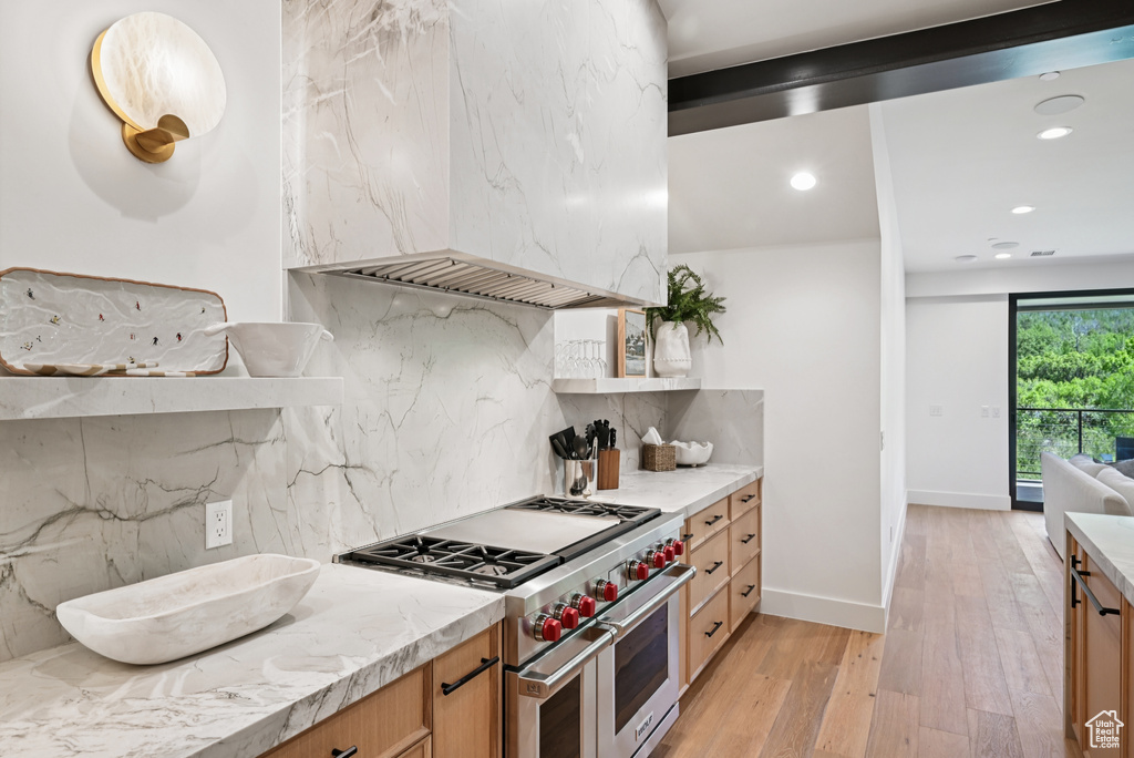 Kitchen featuring double oven range, light wood finished floors, backsplash, light countertops, and custom range hood
