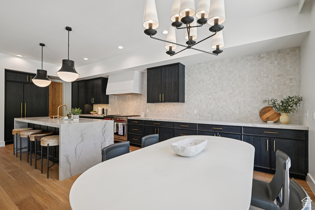 Kitchen featuring wall chimney exhaust hood, high end stove, dark cabinetry, light wood-type flooring, and a breakfast bar area