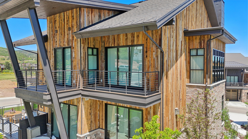 View of side of property with a balcony, roof with shingles, and board and batten siding