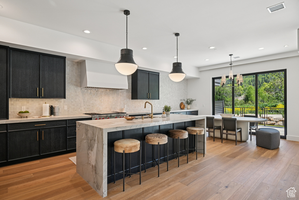 Kitchen with dark cabinets, a sink, premium range hood, light wood-type flooring, and recessed lighting