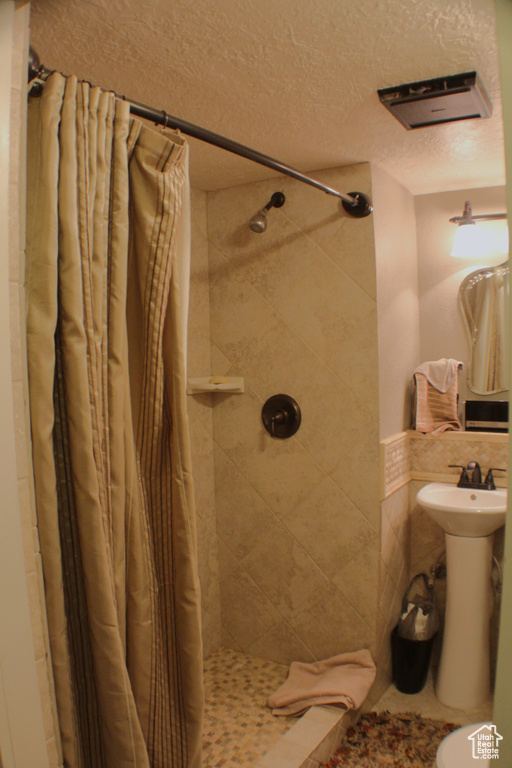 Full bath with a tile shower, a textured ceiling, and toilet