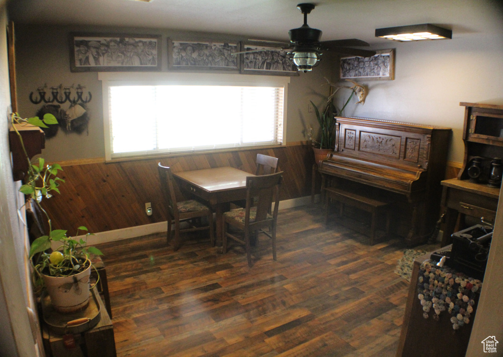 Dining room featuring a wainscoted wall, wood walls, a ceiling fan, and dark wood-style flooring