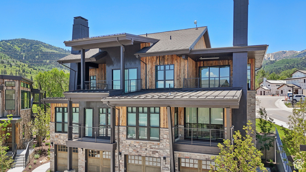 Back of property featuring a balcony, a chimney, a mountain view, and a standing seam roof