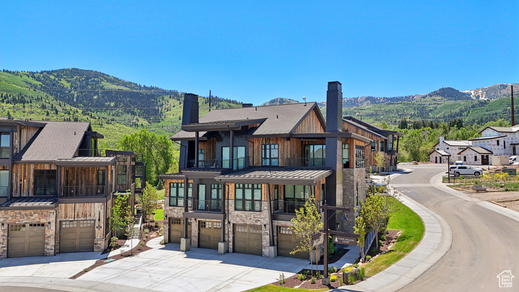 View of front of house with a balcony, a standing seam roof, an attached garage, a chimney, and concrete driveway