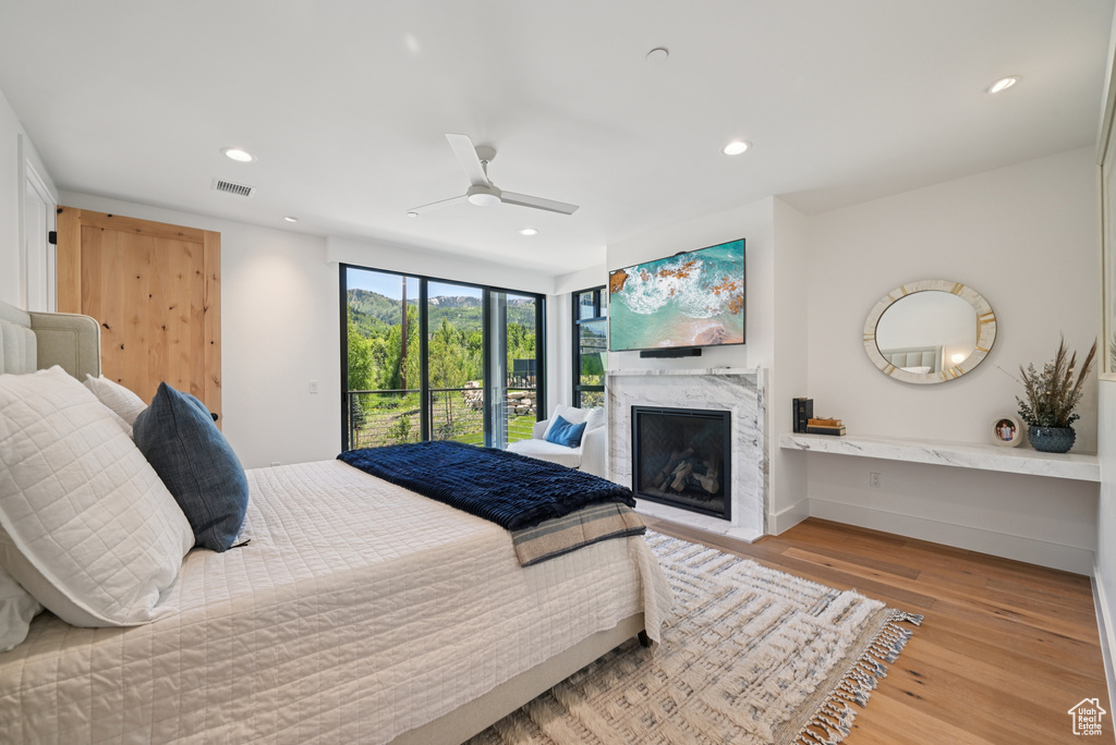 Bedroom with access to exterior, a high end fireplace, wood finished floors, recessed lighting, and ceiling fan