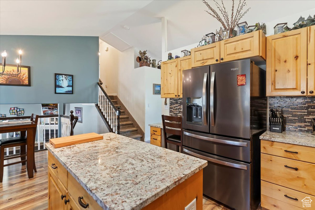 Kitchen featuring stainless steel fridge with ice dispenser, light brown cabinetry, backsplash, a kitchen island, and light stone counters