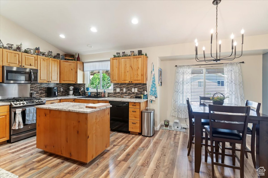 Kitchen featuring appliances with stainless steel finishes, a sink, a chandelier, backsplash, and a kitchen island