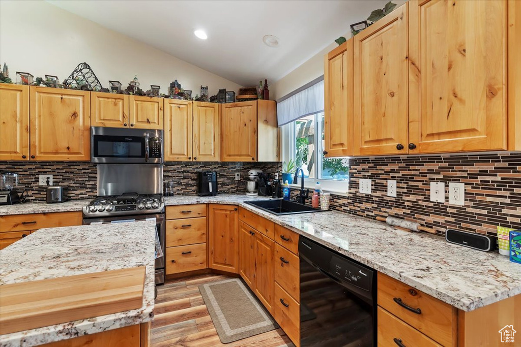 Kitchen with appliances with stainless steel finishes, a sink, light wood-style flooring, vaulted ceiling, and decorative backsplash