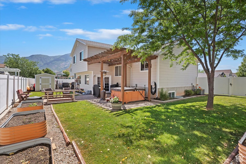 Back of property with a hot tub, a vegetable garden, a mountain view, a patio area, and a pergola