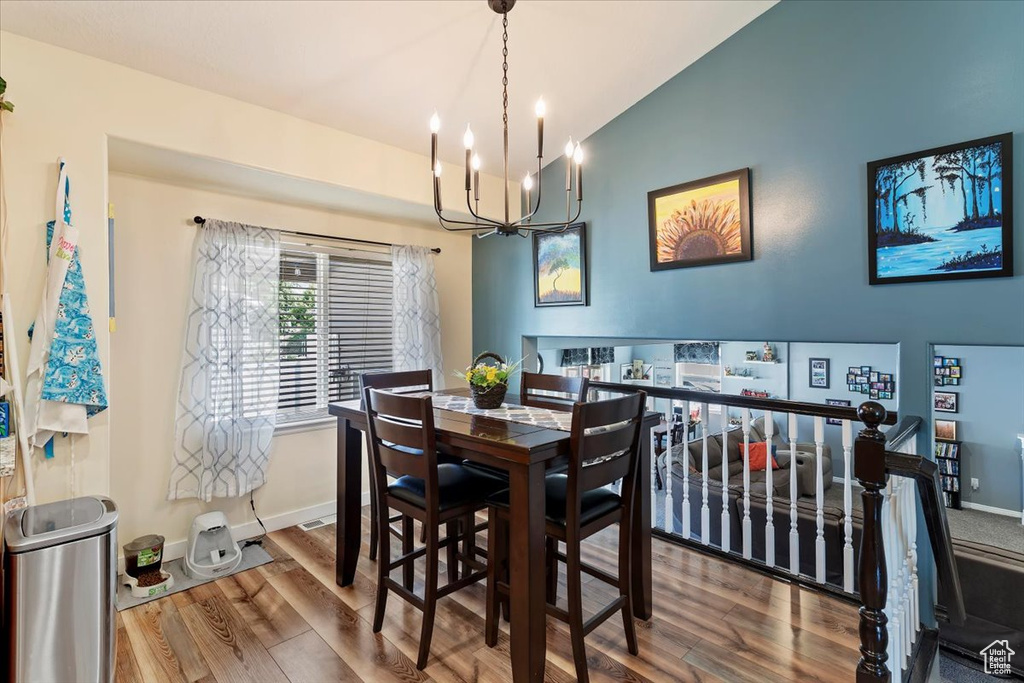 Dining space with vaulted ceiling, a chandelier, wood finished floors, and baseboards