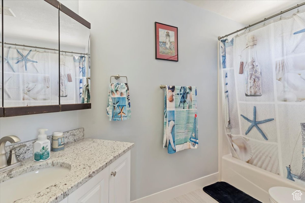 Bathroom with vanity, baseboards, shower / bath combination with curtain, and toilet
