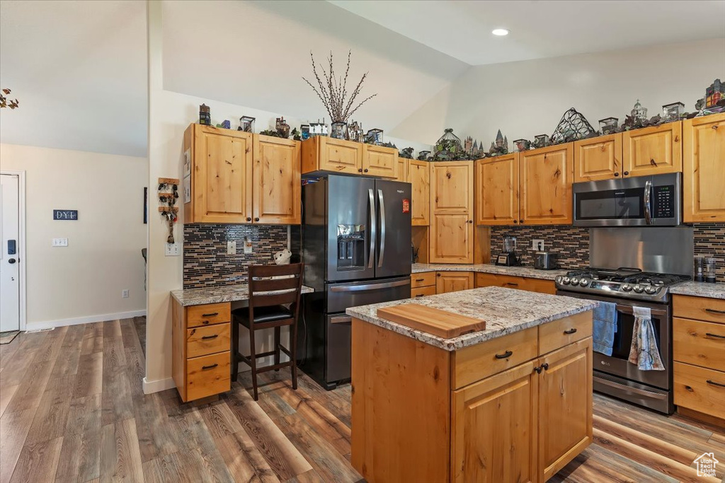 Kitchen with appliances with stainless steel finishes, vaulted ceiling, decorative backsplash, a center island, and light stone countertops