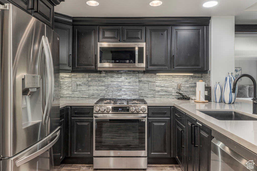 Kitchen with appliances with stainless steel finishes, a sink, light countertops, backsplash, and wood finished floors