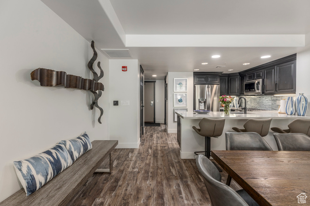 Kitchen featuring appliances with stainless steel finishes, light countertops, a breakfast bar, dark wood finished floors, and recessed lighting