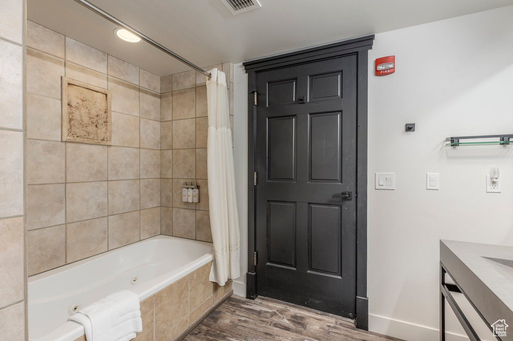 Bathroom featuring a combined bath / shower with jetted tub, wood finished floors, vanity, and baseboards