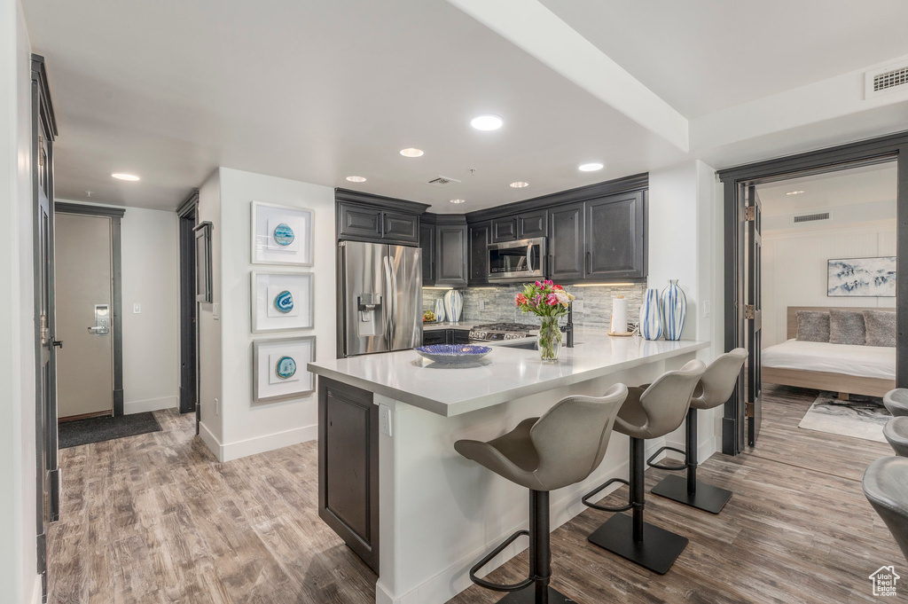Kitchen featuring appliances with stainless steel finishes, light countertops, light wood-style floors, a kitchen bar, and decorative backsplash