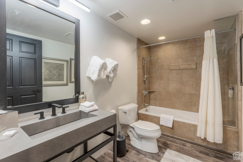 Bathroom with toilet, tiled shower / bath combo, wood finished floors, vanity, and recessed lighting