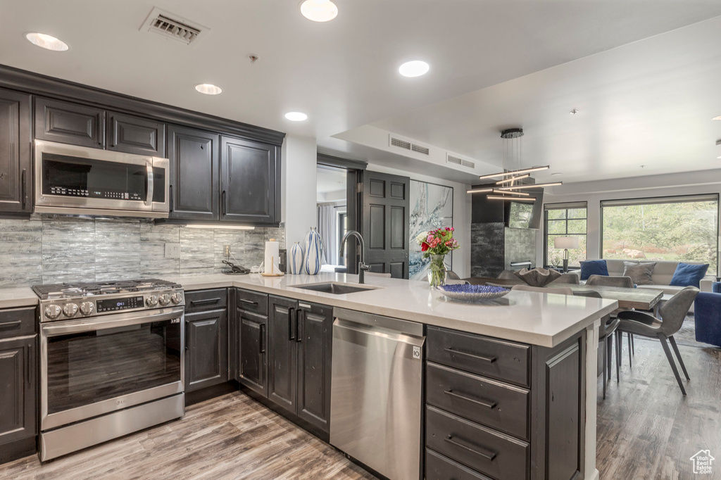 Kitchen with stainless steel appliances, a sink, a peninsula, open floor plan, and light countertops