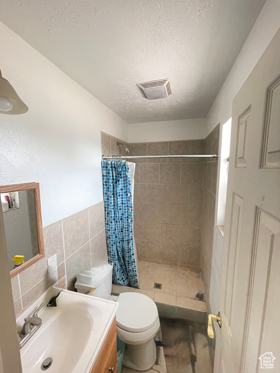 Bathroom featuring a shower stall, vanity, a textured ceiling, toilet, and tile walls