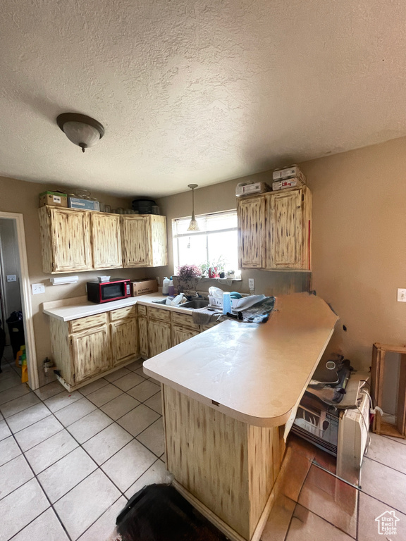 Kitchen with a peninsula, light countertops, light tile patterned floors, a textured ceiling, and pendant lighting