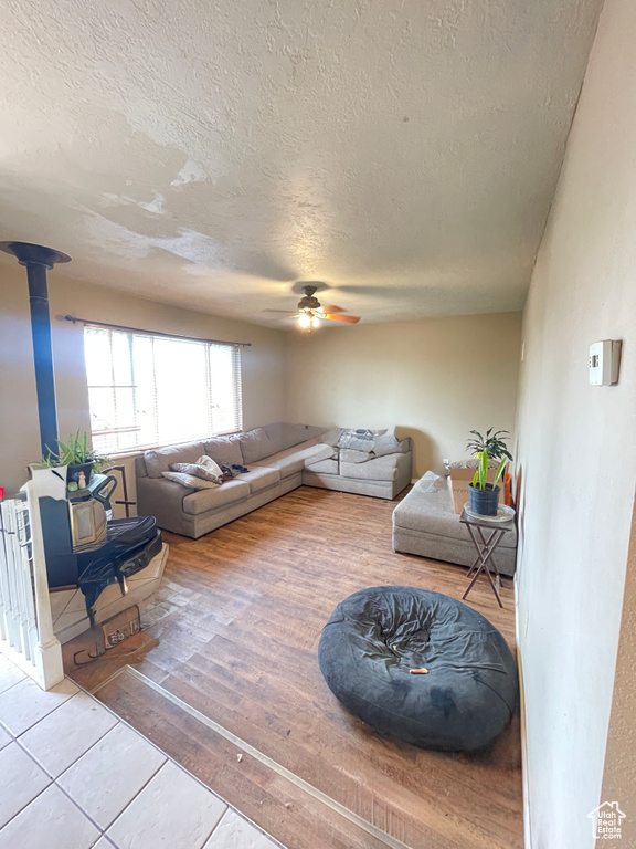 Living room with a textured ceiling, a ceiling fan, wood finished floors, and a wood stove