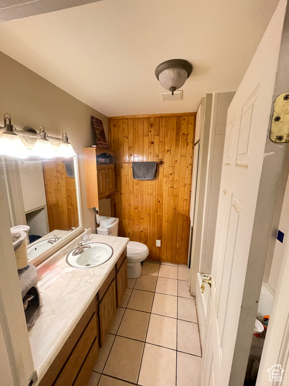 Bathroom with wooden walls, toilet, vanity, tile patterned flooring, and a shower